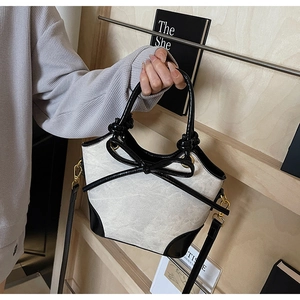 Detail of canvas and black leather bucket bag with bow accent and gold hardware