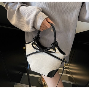 Detail view of mini bucket bag with black patent leather bow and contrast piping finish