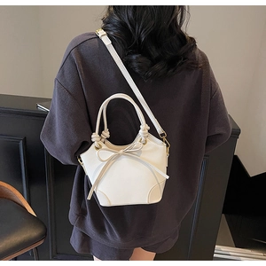 White bucket bag with bow detail shown on shoulder with gold hardware and round handle