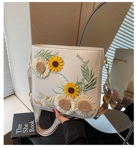 Detail of sunflower and daisy embroidery on a cream shoulder bag with ethnic strap