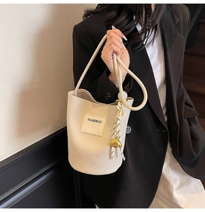 Détail du sac seau beige avec poignée en corde tressée et breloque ours métallique