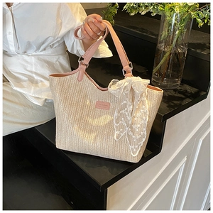 Detail of woven beach tote featuring pink leather handles and delicate lace scarf accent