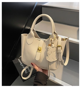 Close-up of cream textured leather handbag featuring golden twist lock and dog charm