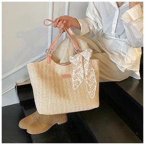 Close-up of woven straw tote bag with pink leather handles and white lace bow detail