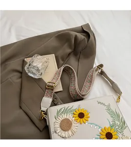 Detail of white leather crossbody bag with sunflower embroidery and woven strap