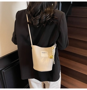 Détail du sac seau beige texturé avec foulard décoratif et pendentif ours doré élégant