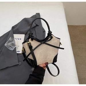 Detail of contrast bucket bag with beige matte fabric, black leather trim, and bow detail