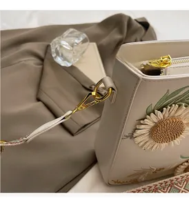 Close-up of sunflower embroidery on beige bucket bag with woven shoulder strap