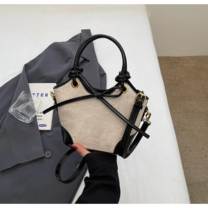 Detail of minimalist canvas bucket bag showing black leather trim and bow decoration