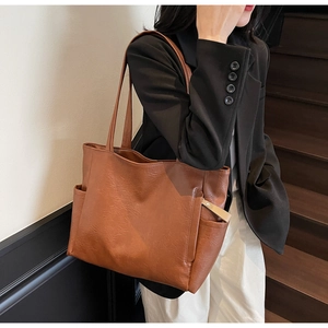 Brown leather tote bag detail featuring pebble texture and side pocket on a model