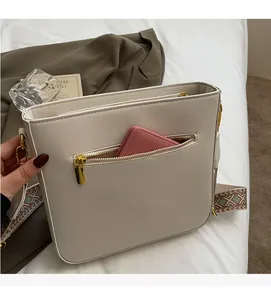 Detail of cream crossbody bag featuring front zipper pocket with a pink wallet inside
