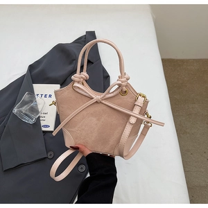 Detail of pink faux suede bucket bag featuring a bow and round handle held by a model