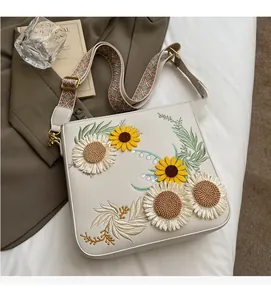 Detail of sunflower embroidery on off-white crossbody bag with colorful woven strap