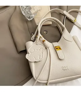 Detail of off-white lychee leather day bag with gold twist lock and dog charm pendant