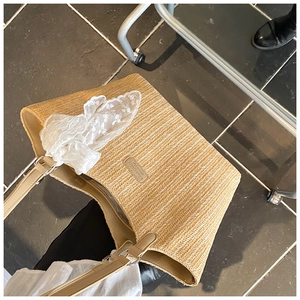 Detail view of woven straw tote bag featuring a large white lace bow and leather strap