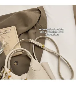 Detail of beige lychee leather handbag featuring gold M-logo charm and adjustable strap