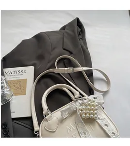 Dettaglio borsa bowling in pelle crema con cuciture a cuore e logo sopra un blazer