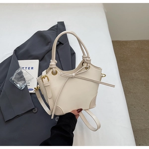 Detail of cream white bucket bag featuring leather bow accent and knotted handle design