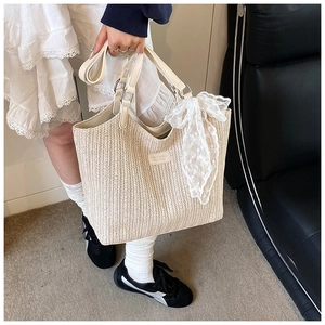 Close-up of a cream woven tote bag with a white lace bow and leather handles