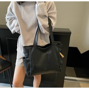 Close-up of black leather tote bag with functional side pocket and fine litchi grain texture