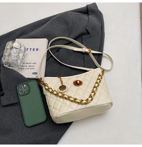 Detail of white quilted tote bag with golden chain and twist lock on a grey suit jacket
