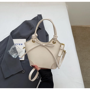 Detail of cream trapezoid handbag with decorative bow and elegant gold hardware
