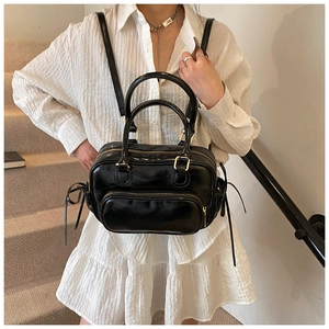 Detailed view of black high-gloss backpack with top handle worn on model in minimalist setting