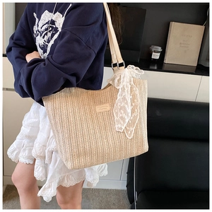 Close-up of beige woven straw tote bag featuring delicate white lace bow and leather logo