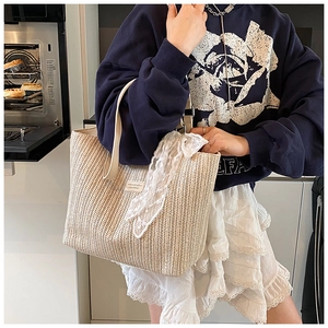 Detail of woven straw tote bag featuring white lace ribbon and rectangle logo patch
