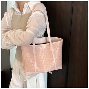 Détail du cabas rose tissé avec plaque logo dorée porté par un mannequin en chemise blanche