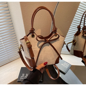 Detailed close-up of a vintage beige canvas bucket bag with brown leather trim and bow