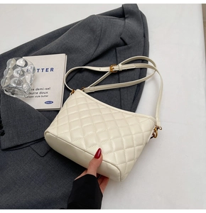 Close-up of white quilted crossbody bag with gold buckle on grey blazer suit background
