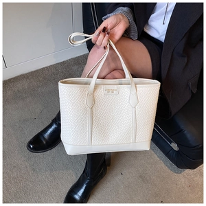 Gros plan sur la texture tissée blanche et le logo doré d'un grand sac cabas chic