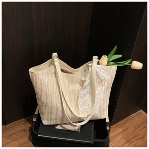 Close-up of woven straw tote bag featuring cream leather straps and delicate lace scarf