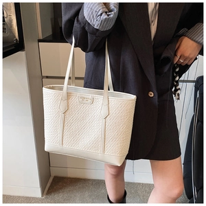Détail d'un sac cabas tissé beige montrant la surface texturée et les longues bandoulières