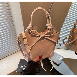 Close-up of pink suede bucket bag featuring a decorative bow and bronze metal hardware