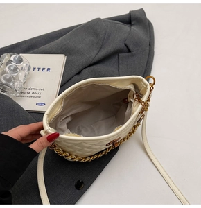 Detail view of cream quilted shoulder bag with gold chain strap on grey blazer