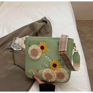 Detail of floral embroidery on light green leather crossbody bag with wide patterned strap