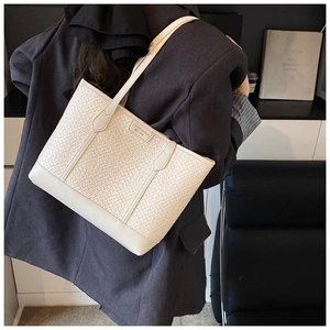 Détail de la texture tissée et du logo métallique sur un grand sac cabas blanc