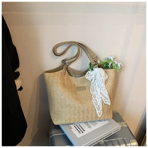 Detail of woven straw tote bag with brown leather handles and white lace bow decoration