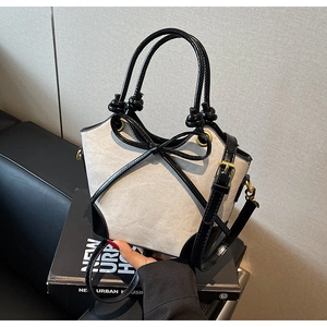 Close-up of canvas bucket bag with leather bow, knot handle and golden metal buckles