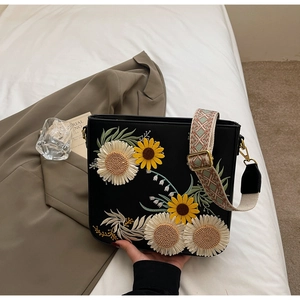 Detail of floral embroidery on a black crossbody bag with woven shoulder strap