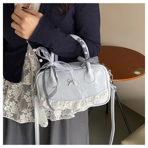 Detail of light blue Boston bag featuring white lace trim and bow charm accent