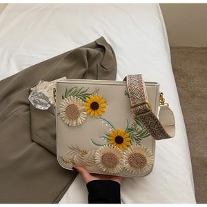 Detail of white leather bucket bag with sunflower embroidery and woven guitar strap