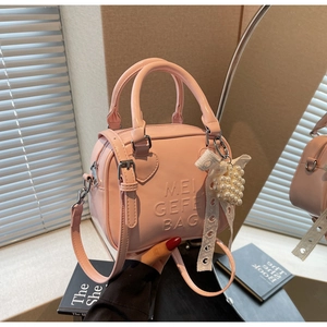 Dettaglio borsa Boston rosa chiaro con fiocco in pizzo, ciondolo di perle e anelli a cuore
