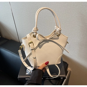 Detail of white PU leather bucket bag featuring a large bow and gold hardware accents
