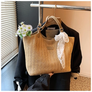 Detailed close-up of woven straw tote bag featuring a decorative lace scarf and leather patch