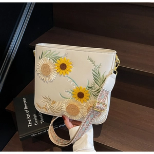 Close-up of cream white bucket bag featuring floral sunflower embroidery and woven strap