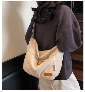 Detail of canvas messenger bag featuring a brown leather patch and wide shoulder strap