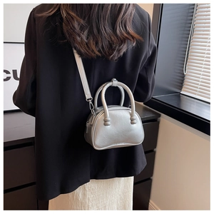 Detail of silver metallic semi-round crossbody bag with dual circular handles on model